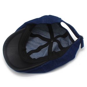 Detail of dark blue denim newsboy cap with leather brim bottom and adjustable metal strap