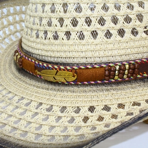 Detailed close-up of straw cowboy hat featuring golden feather pendant and beaded hatband