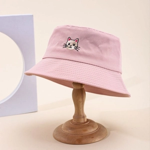 Pink cotton bucket hat with cartoon cat embroidery displayed on a wooden stand