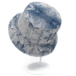Blue and white reversible bucket hat with vintage landscape patterns on a white stand