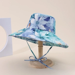 Dettaglio di cappello solare a fiori blu con tesa larga e cordino abbinato a fiocco decor