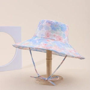 Dettaglio del cappello a secchiello floreale con motivi tenui e laccio antivento