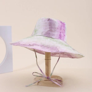 Dettaglio cappello da sole tie-dye con tesa larga e cordino regolabile su supporto in legno