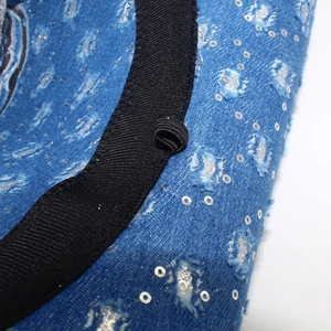 Detail of blue denim cowboy hat with distressed holes, sequins and internal elastic band