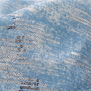Dettaglio del tessuto denim blu chiaro con file di paillettes argentate e brillanti