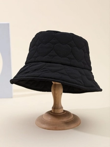Detail of heart-shaped quilted stitching on a black bucket hat placed on a wooden stand