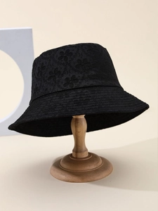 Detailed view of black bucket hat with intricate floral lace texture on a wooden stand