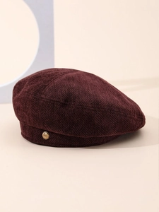 Detail of burgundy herringbone beret with a gold L'AMOUR badge and textured fabric