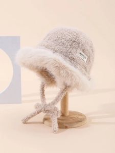 Detail of warm beige plush bucket hat featuring a woven patch and fuzzy faux fur brim