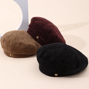 Three elegant corduroy beret hats in brown, burgundy, and black with golden metal button detail