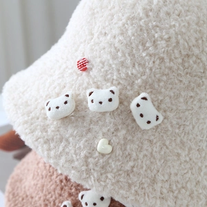 Detailed close-up of soft beige fleece bucket hat with cute bear patches and heart button