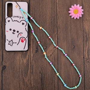 Detail of mint green beaded phone lanyard with colorful heart charms on a desk