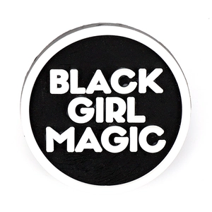 Detail of round PVC shoe charm with white 'BLACK GIRL MAGIC' 3D raised text on black background