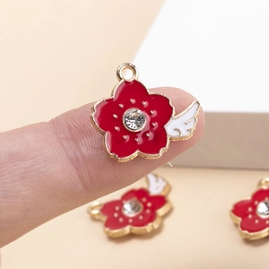 Detailed close-up of red flower heart charm with zircon and white wing in hand