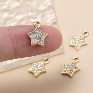Detailed macro of tiny gold star pendants with colorful rhinestones held by a finger