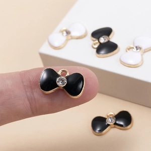 Macro detail of tiny bow pendants featuring gold plating and enamel inlay on a fingertip
