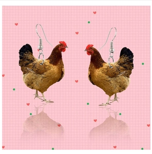 Detail shot of realistic hen pendant earrings with silver hooks on acrylic surface