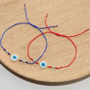 Bracelets tressés réglables mauvais œil en rouge et bleu sur un plateau en bois