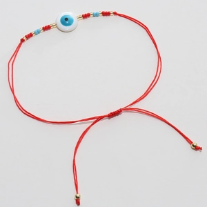 Détail du bracelet Evil Eye en cordon rouge tressé avec nœud coulissant et perles d'or