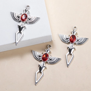 Vue détaillée du pendentif croix avec ailes argentées et pierre précieuse rouge au centre