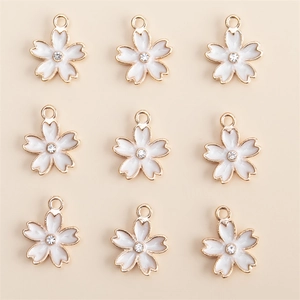 Détails de neuf breloques fleurs de cerisier dorées avec émail blanc et cristal au centre