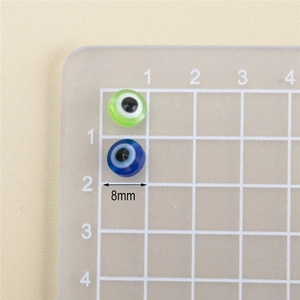 Macro detail of 8mm resin evil eye beads in green and blue on a measurement grid