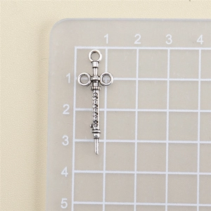 Detail showing an antique silver syringe pendant on a measuring grid for size reference