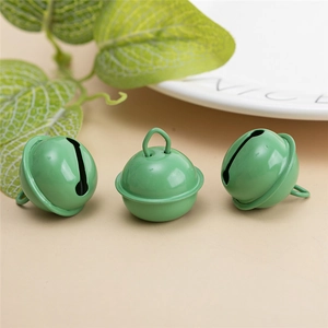 Trois cloches métalliques vertes laquées avec boucles de suspension sur fond beige clair