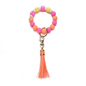 Close-up of silicone beaded keychain with XOXO letters, orange tassel and gold clasp