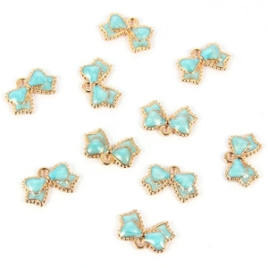 Macro shot of ten light blue enamel bow charms with golden metal edges for DIY jewelry making