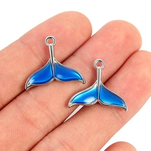 Macro shot of two gradient blue enamel mermaid tail charms held in a hand for scale