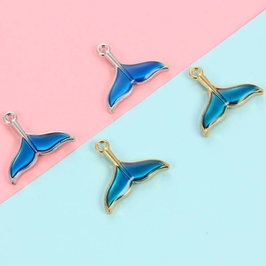 Close-up of enamel mermaid tail charms with blue gradient and gold or silver edges