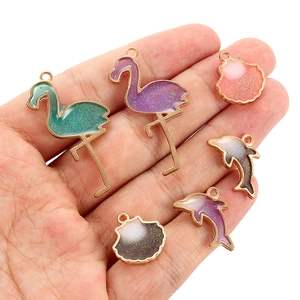 Detail of glitter enamel flamingo and shell charms held in hand for scale and texture