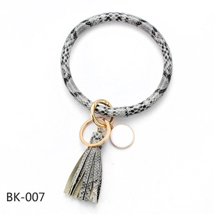 Detail of snake skin print PU leather bangle keychain with golden ring and enamel pendant