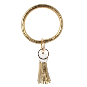 Detail eines goldenen Lederarmband-Schlüsselanhängers mit weißen Scheiben und Fransenquaste