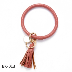Close-up of pink faux leather bangle keychain with gold metal ring and tassel detail