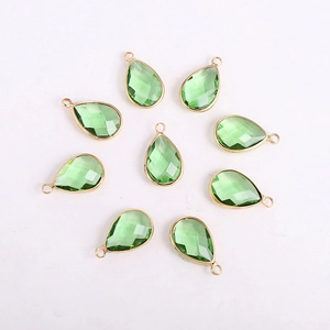 Macro view of green teardrop glass charms with gold metal edges for DIY jewelry making