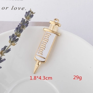Detailed close-up of golden syringe charm with white enamel on a decorative white tray