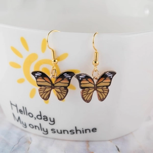 Detail of butterfly drop earrings on a ceramic cup with yellow and black resin patterns