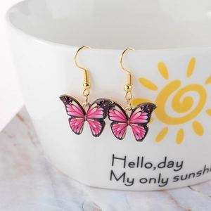 Detail view of colorful butterfly earrings hanging on a white ceramic cup with gold hooks