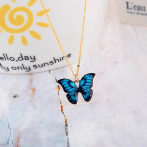 Macro detail of a gradient blue butterfly pendant on a gold chain over a white artistic mug