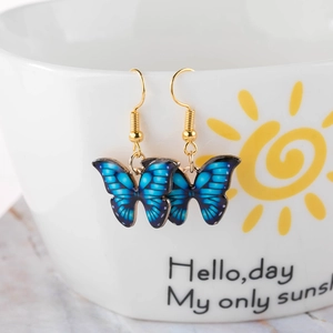 Blue butterfly drop earrings hanging on a ceramic cup edge with gold hooks