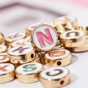Macro-opname van kleurrijke emaille letterkralen met gouden randen voor doe-het-zelf