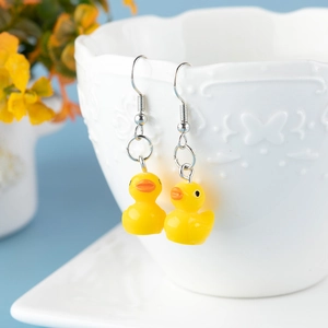 Close-up of cute yellow duck dangle earrings hanging on a white decorative porcelain cup