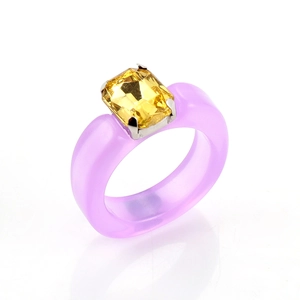 Macro view of a purple resin ring with a large rectangular yellow crystal in silver claw setting