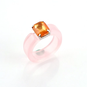 Detail of a pink resin ring featuring a rectangular orange gemstone in a silver claw setting