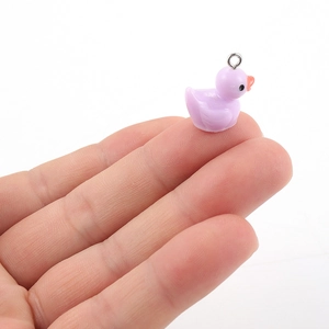 Close-up of a tiny purple resin duck charm held on a fingertip for size scale