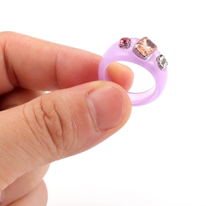 Detalle de anillo de resina púrpura con piedras de ámbar y rosa mostrado en el dedo