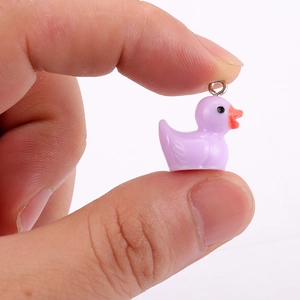 Miniature lavender resin duck pendant with metal ring held between fingers for scale