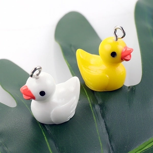 Close-up of yellow and white resin duck pendants with metal rings on green leaves
